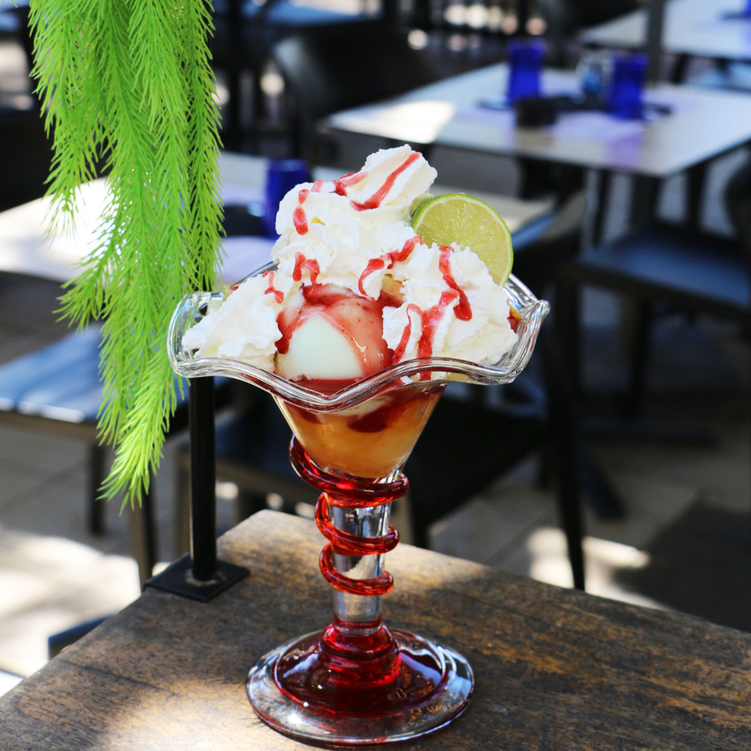 Vue sur une coupe de glace dans les tons orange et rouge avec chantilly et citron vert, le Yacht Café, crêperie Carnon.
