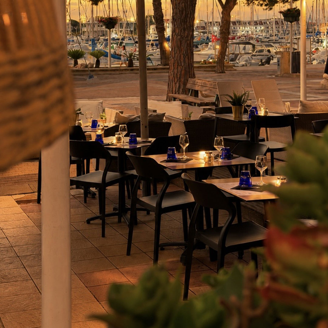 Vue sur la terrasse extérieure du restaurant Carnon, le Yacht Café, avec coucher du soleil & les bateaux en arrière plan.